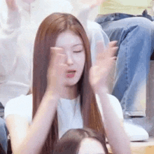 a woman with long hair is clapping her hands while sitting in a stadium .