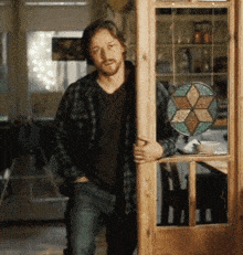 a man in a plaid shirt leans against a door