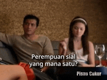 a man and a woman are sitting on a couch and the woman says perempuan sial yang mana satu ?