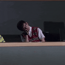a man wearing glasses and a vest is sitting in front of a monitor