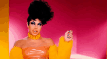 a drag queen is wearing a yellow fur coat and a pink background .