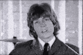 a young man in a suit and tie is standing in front of a window in a black and white photo .