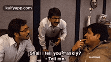 three men are talking to each other in a room and one of them is smoking a cigarette while the other two are talking .