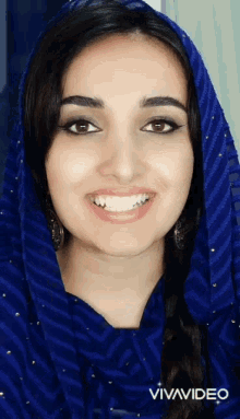 a woman wearing a blue scarf and earrings smiles for the camera
