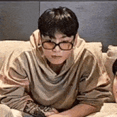 a man wearing glasses is sitting on a couch holding a remote control .