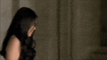a woman with long dark hair is standing in a dark room