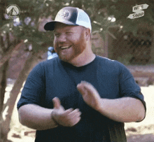 a man with a beard wearing a hat is clapping his hands