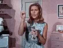 a woman is holding a glass of water in her hand in a pink room .