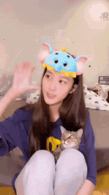 a woman wearing an elephant headband holds a cat in her lap
