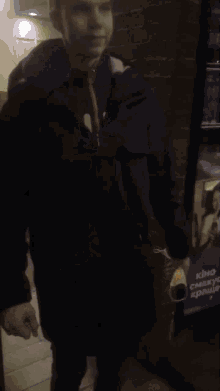 a man in a black jacket sits in a dark room with a barrel in the background