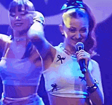 a woman is singing into a microphone on a stage while another woman stands behind her .