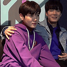 two young men are sitting next to each other and one of them is wearing a purple hoodie