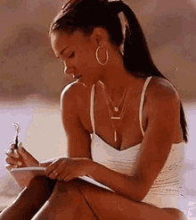 a woman in a bikini is sitting on the beach writing in a notebook .