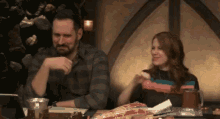 a man and a woman are sitting at a table with pizza and beer .
