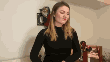 a woman in a black sweater is standing in front of a wall with clothes on it
