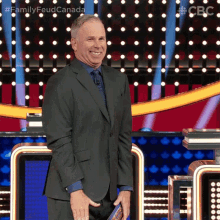 a man in a suit and tie stands in front of a podium with a sign that says family feud canada on it