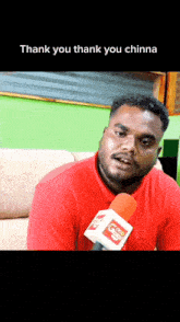 a man in a red shirt is talking into a microphone with the words thank you thank you chinna written below him