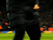 a man is dancing on a soccer field while wearing a jacket that says ' liverpool ' on it