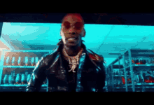 a man wearing sunglasses and a leather jacket is standing in front of a screen in a room .