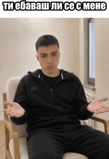 a man in a black nike jacket sits in a chair with his hands outstretched
