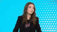a woman in a black jacket stands in front of a blue background with hearts on it