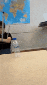 a bottle of aquafina water sits on a table in front of a map of the world