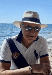 an older man wearing a hat and polo shirt is sitting on the beach