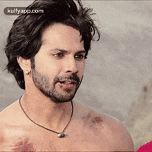 a shirtless man with a beard wearing a necklace and earrings is standing on a beach .