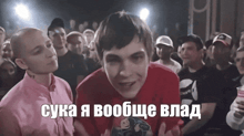 a man in a red shirt stands in front of a crowd with russian writing on the bottom