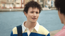 a young man with curly hair wearing a blue and yellow striped shirt