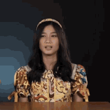 a woman wearing a headband and a colorful shirt is sitting at a table and making a funny face .