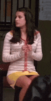 a woman wearing a white sweater and a yellow skirt is sitting on a chair