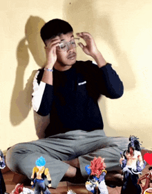 a man wearing glasses sits on the floor with a bunch of action figures
