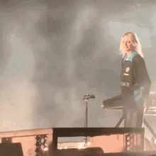 a woman stands on a stage in front of a microphone wearing a blue shirt that says ' x '