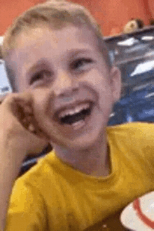 a young boy in a yellow shirt is laughing with his mouth open