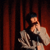 a man is standing on a stage holding a microphone in front of a red curtain .
