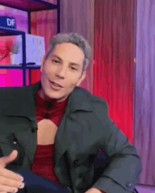 a man wearing a green jacket and a red shirt is smiling