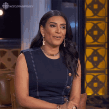 a woman is sitting in front of a wall with the words #cbcdragonsden on it