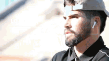 a man with a beard wearing a hat and ear buds looks to the side