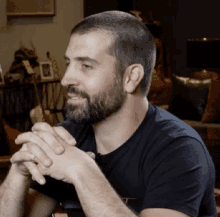 a man with a beard and a ring on his finger is sitting with his hands folded