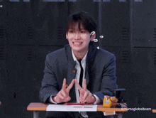 a young man in a suit and tie is sitting at a desk making a funny face