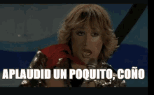 a woman is singing into a microphone with the words aplaudid un poquito cono written on the screen behind her .