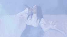 a woman singing into a microphone while wearing a white shirt