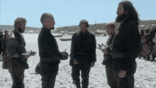 a group of men standing on a sandy beach talking to each other