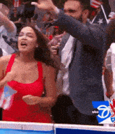 a man in a suit and a woman in a red dress are standing next to each other in a crowd .