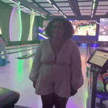 a woman in a white dress stands in a bowling alley in front of a screen that says ' strike ' on it