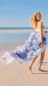 a woman in a blue and white dress stands on the beach next to a swing