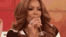 a woman is sitting at a table drinking from a glass .