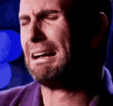 a man with a beard is crying with his eyes closed and a purple shirt on .