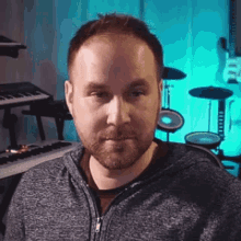 a man with a beard is sitting in front of a drum set and a keyboard .